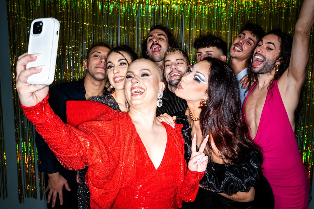 Bald transgender woman taking a selfie with queer, non-binary, gay and lesbian friends at a party 